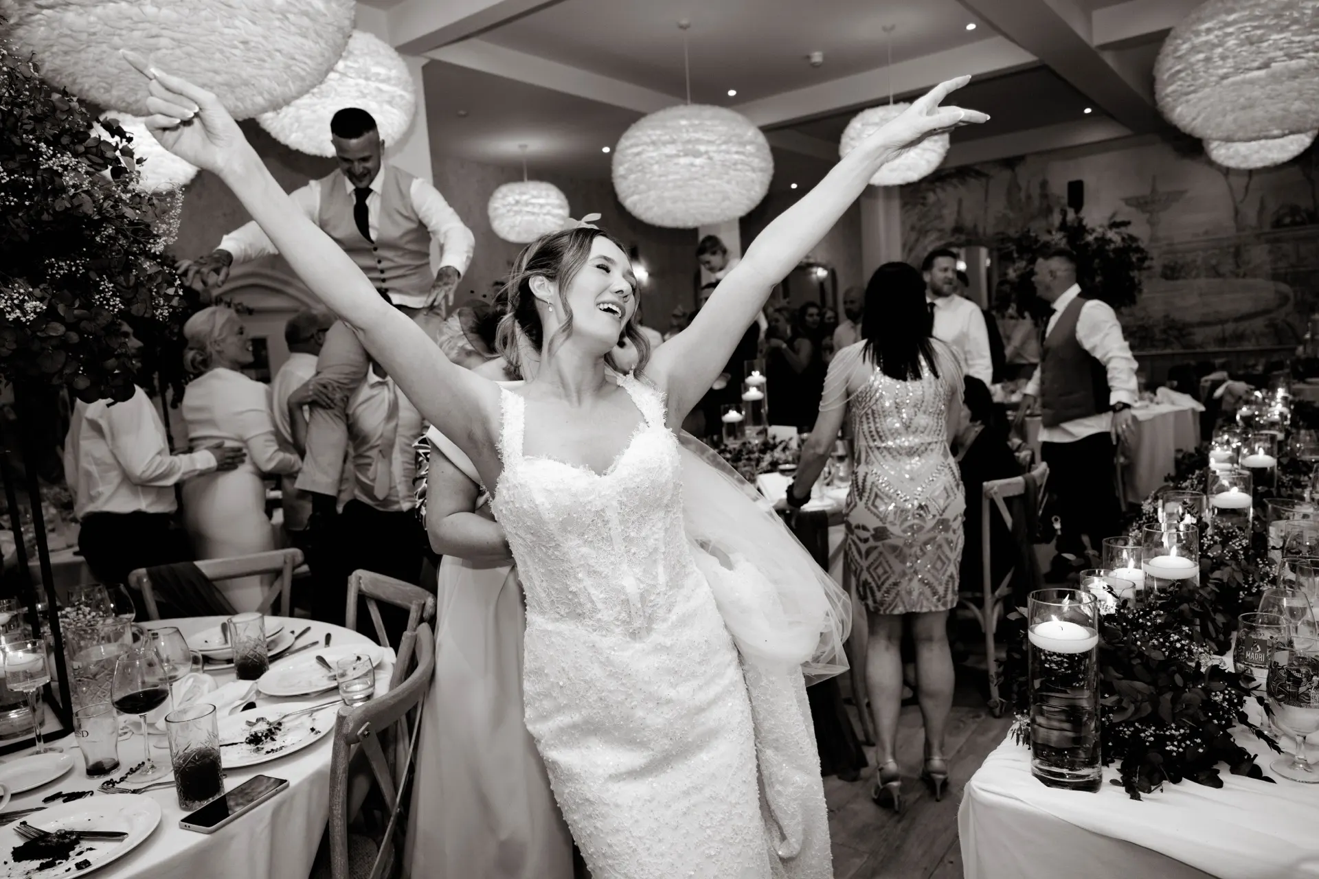 A bride on her feet at the wedding breakfast, arms in the air