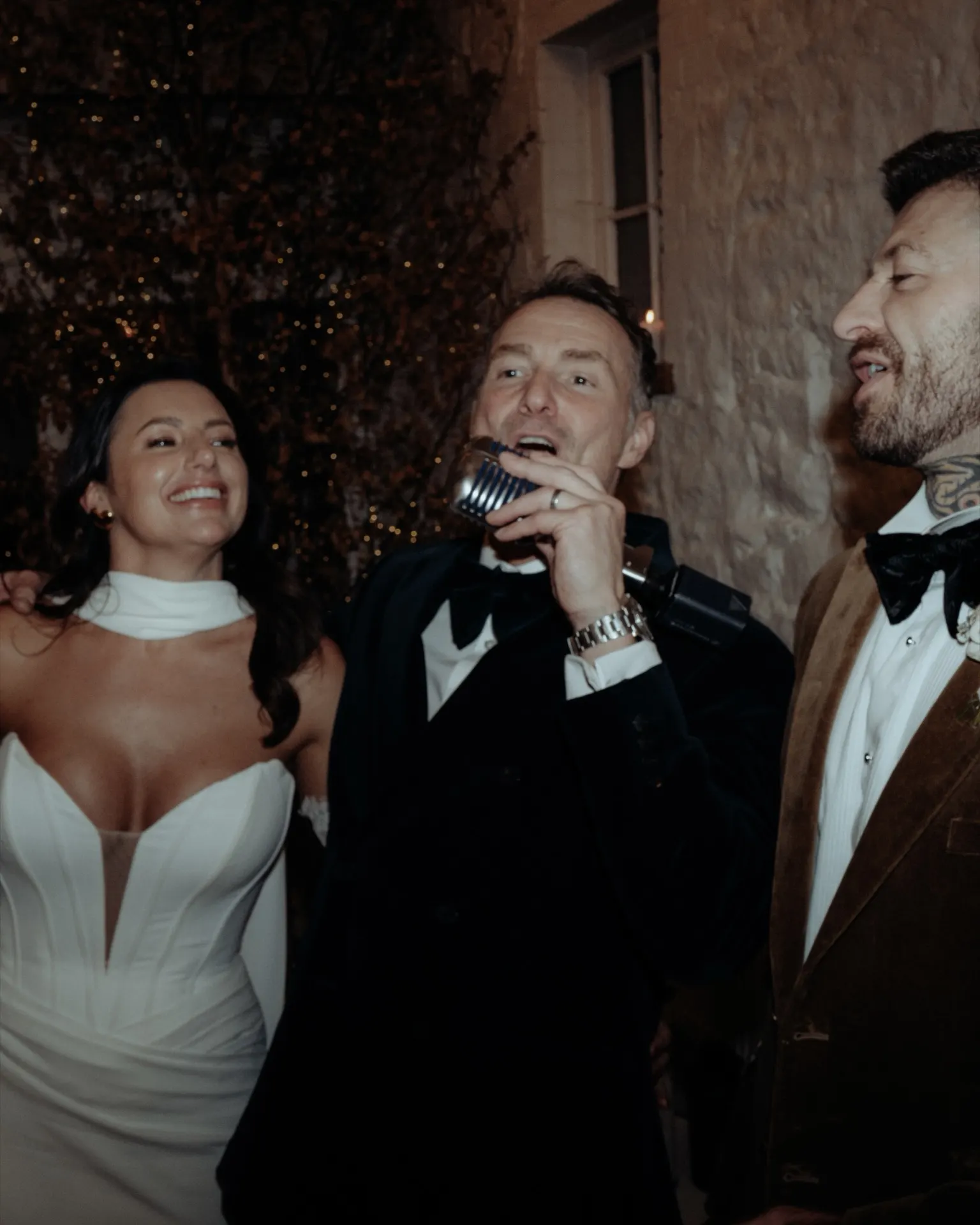 A bride and groom singing with Howard under the evening lights
